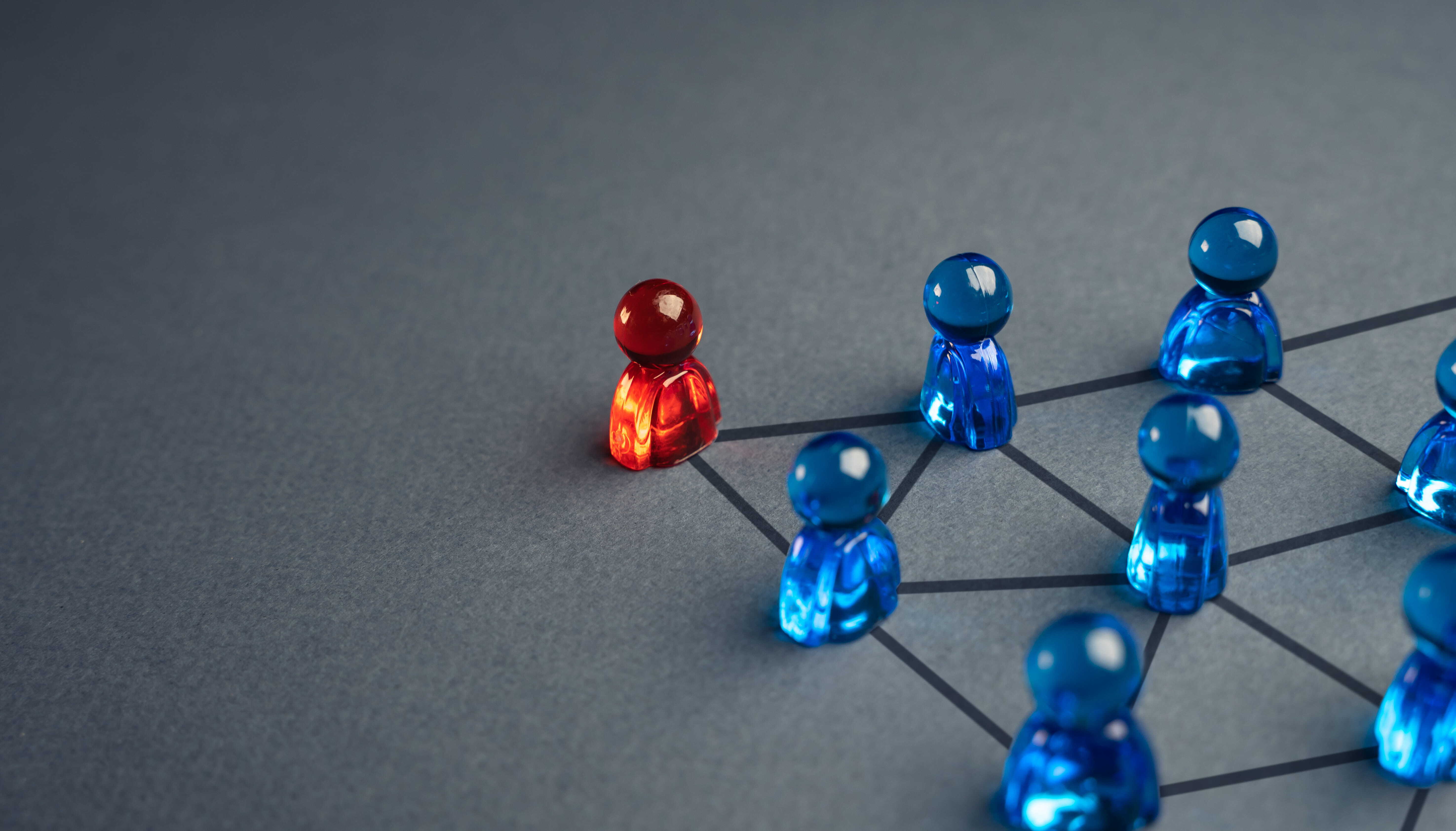 A red figurine positioned within a network of connected blue figures, illustrating the role of a board advisor in navigating complex organisational relationships and stakeholder dynamics.