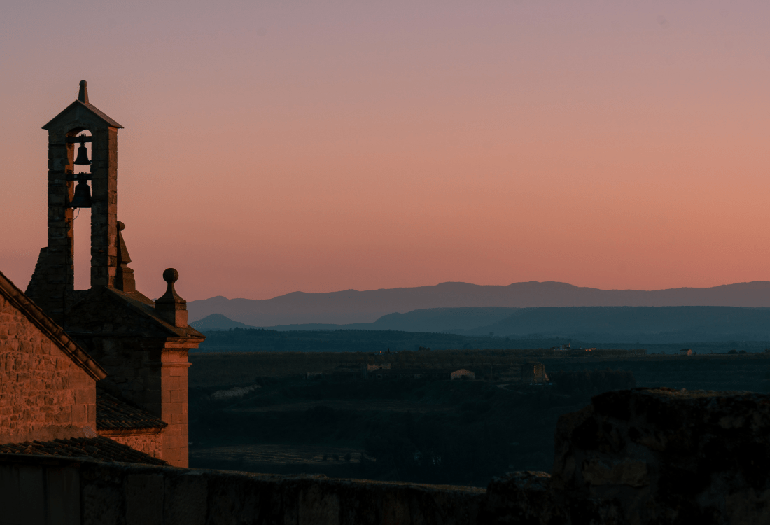 A stone church tower with bells overlooking a valley at sunset, symbolising how organisational culture is shaped by the surrounding landscape and paths taken.